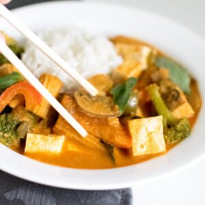 chop sticks pricking up Thai red curry vegetables from a plate.