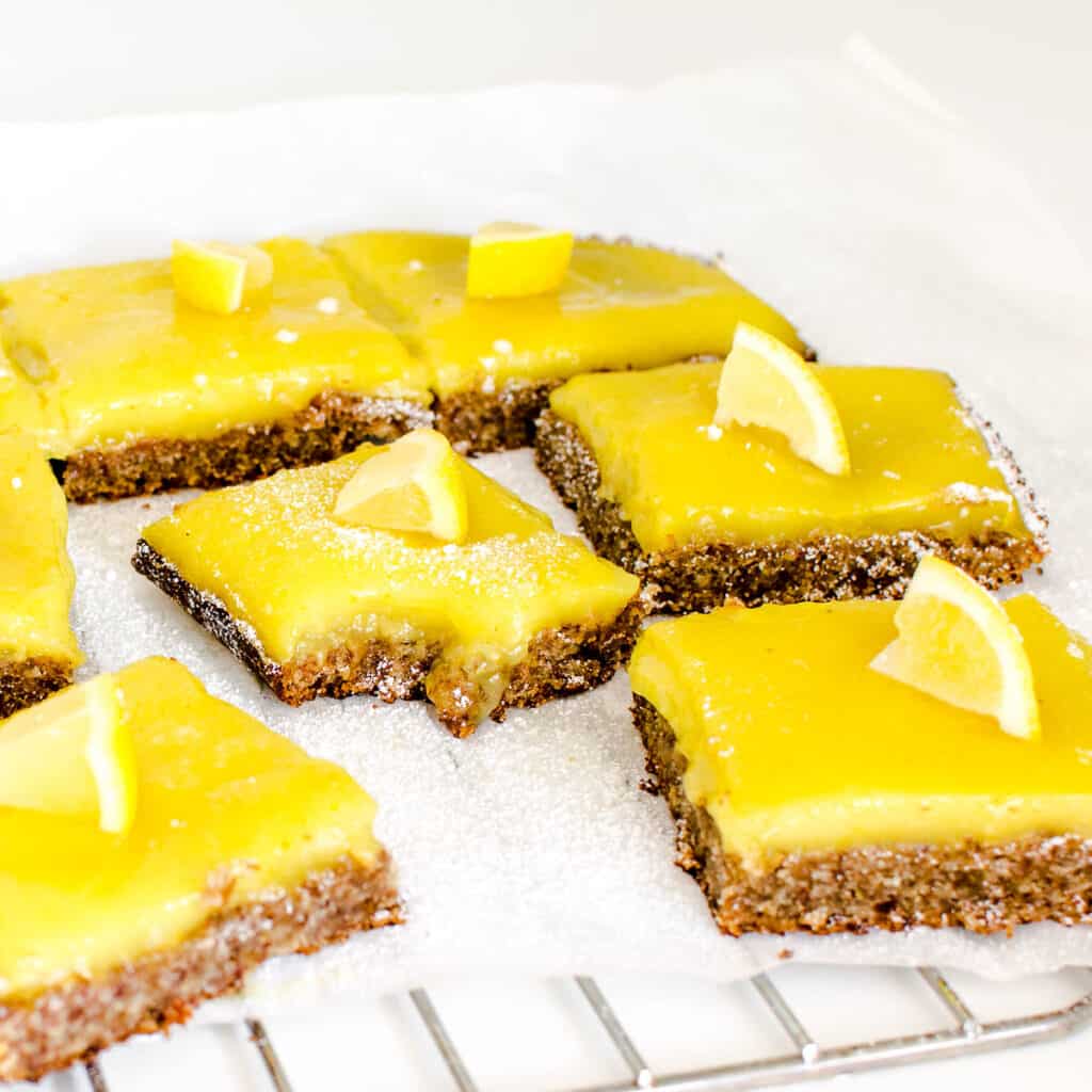 a front view of vegan lemon bars on a parchment paper with a half eaten slice in the middle.