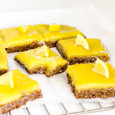 a front view of vegan lemon bars on a parchment paper with a half eaten slice in the middle.