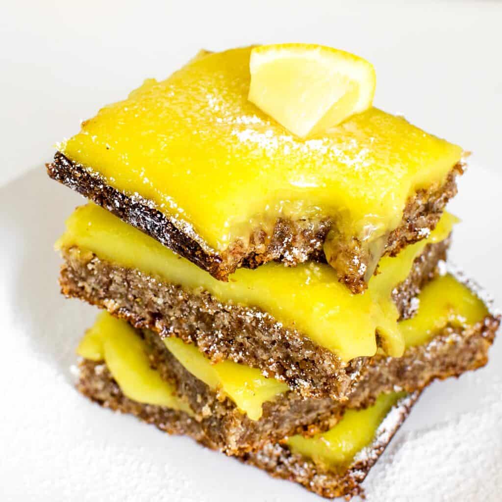 a 45 degree angle view of stacked vegan lemon bars with a half eaten slice at its top.