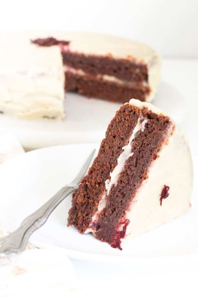 sliced vegan red velvet cake with the entire cake at its background. 