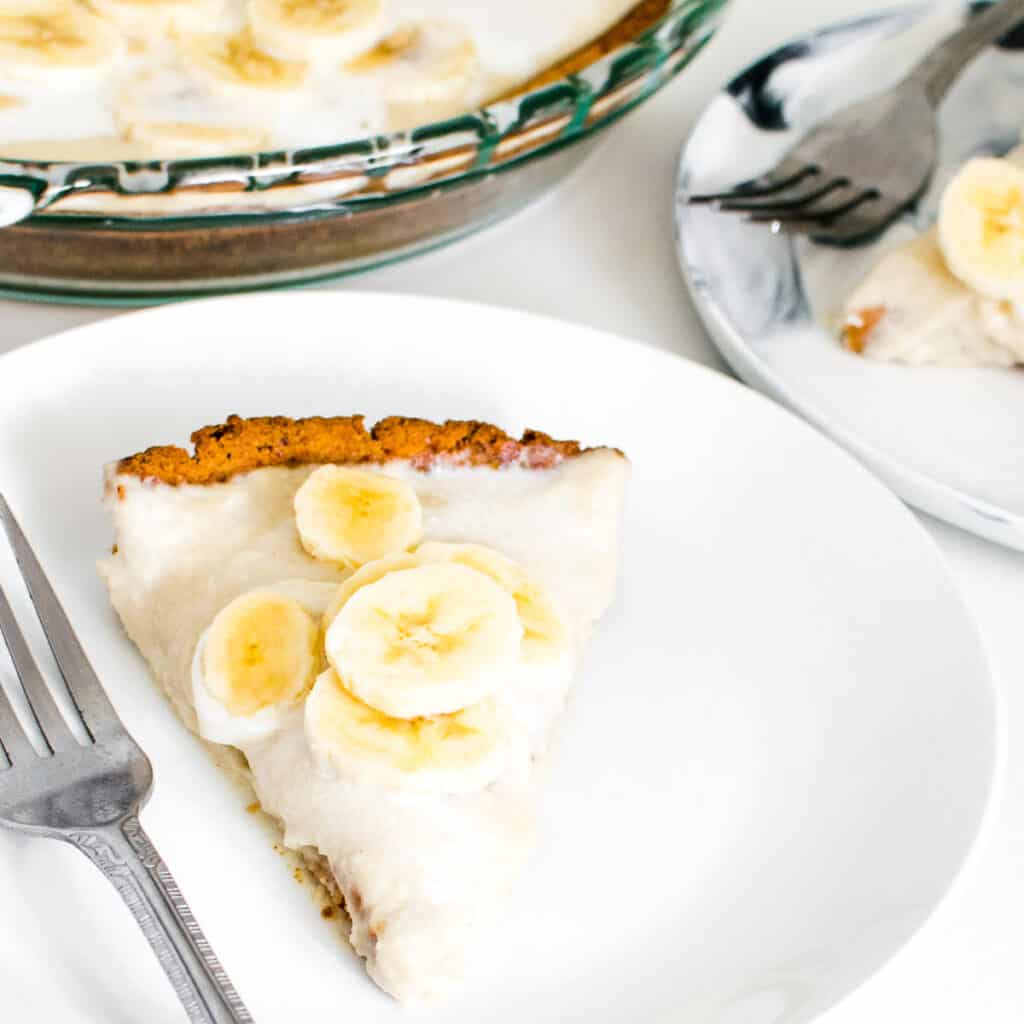 a 45 degree angle view of the vegan banana cream pie in a serving plate along with the whole pie at the backdrop.