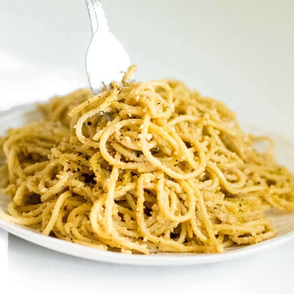 a fork picking up vegan cacio e pepe from the serving plate.