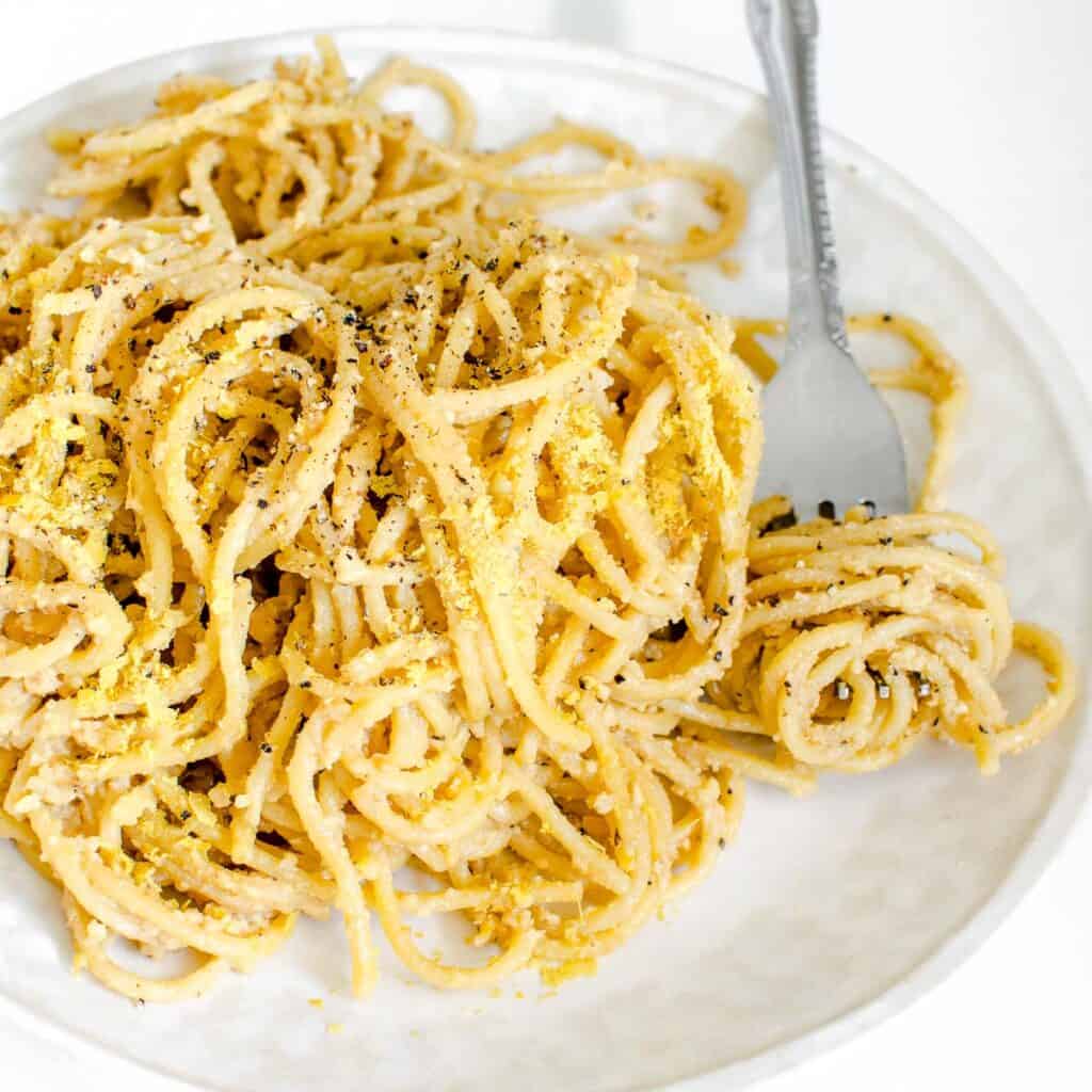 a 45 degree angle view of fork rolled over heaped vegan cacio e pepe.