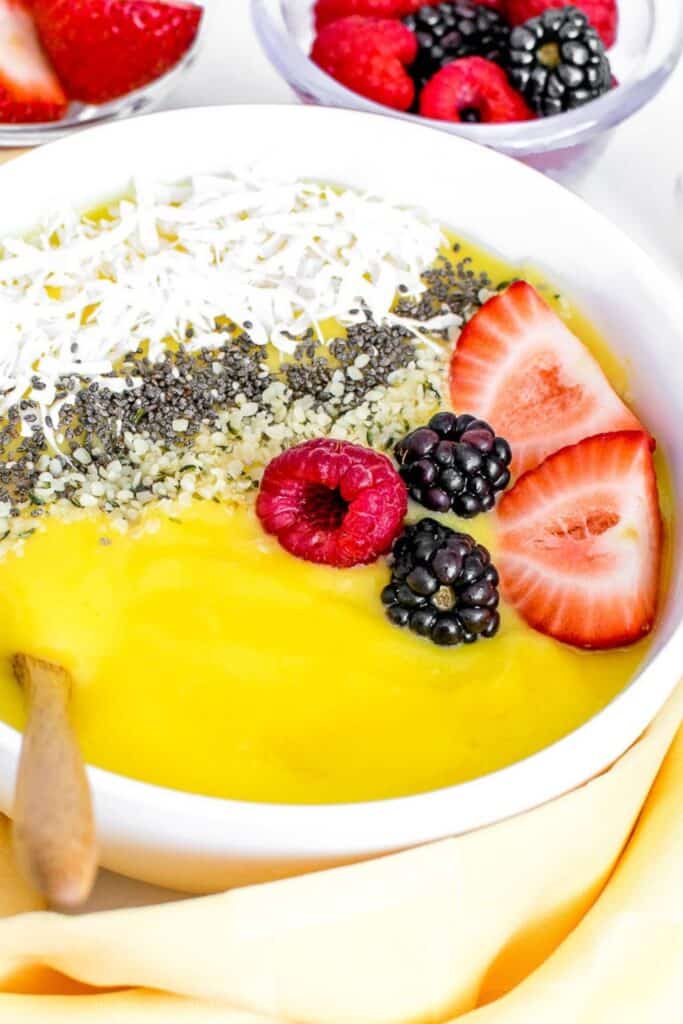 a 45 degree angle close up view of mango smoothie bowl with a wooden spoon.