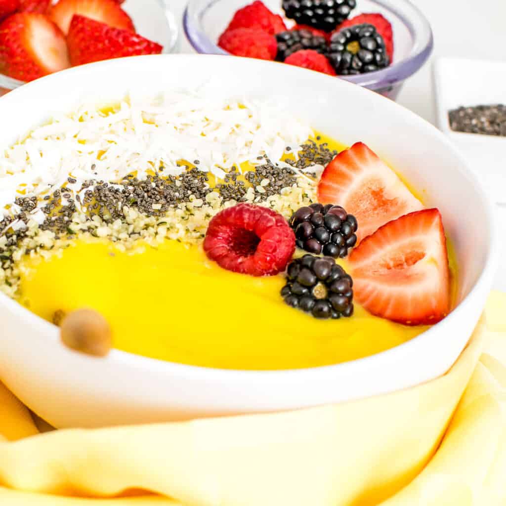 a close up view mango smoothie bowl with a spoon inserted.