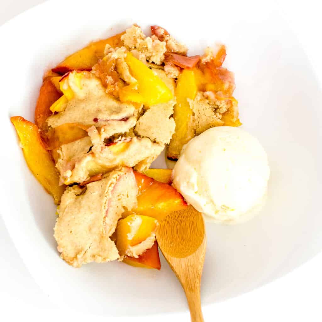 vegan peach cobbler in a bowl served with ice cream.