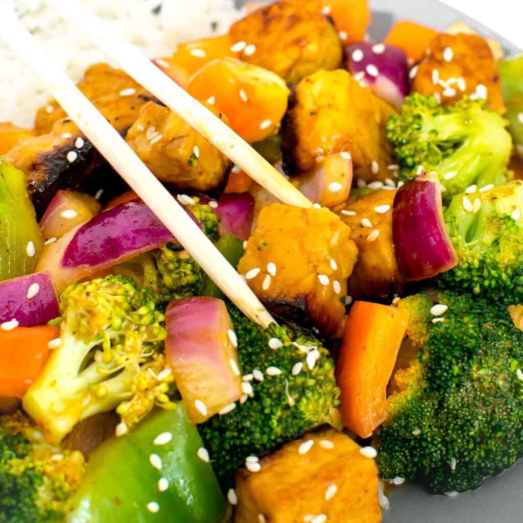 a close up view of chopsticks picking up tempeh stir fry