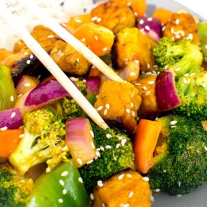 a close up view of chopsticks picking up tempeh stir fry