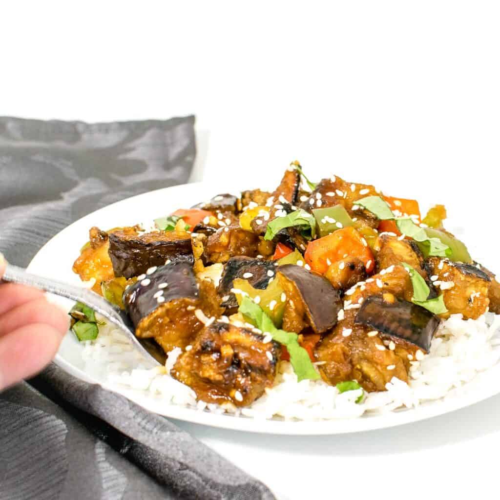 a hand using a fork to dig into eggplant stir fry.