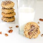 focus on a vegan pecan cookie with a glass of milk and some stacked at the background.