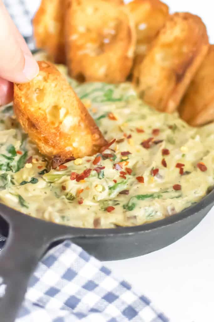 baguette dipping into spinach artichoke dip. 