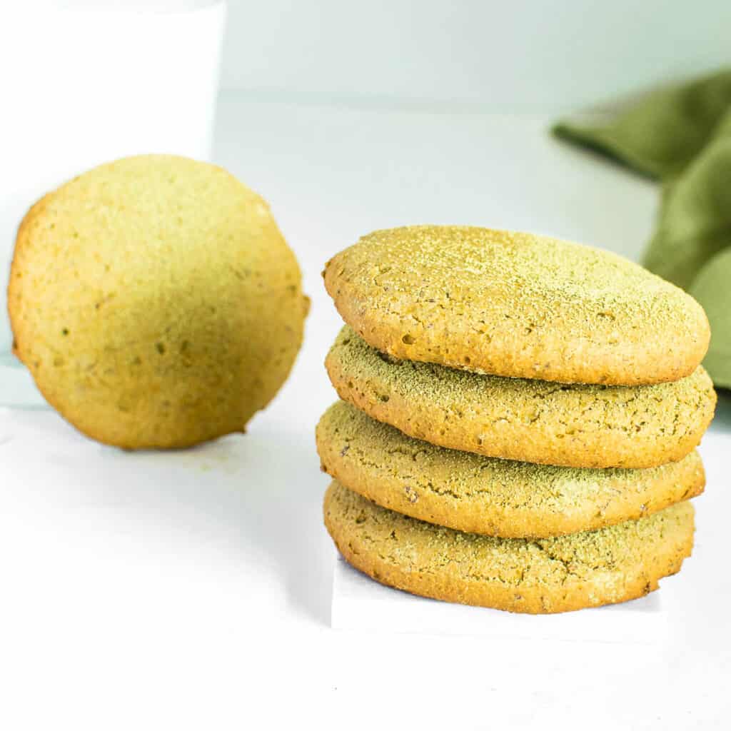 front view of stacked matcha cookies with one cookie at the far end leaning over a glass of milk.