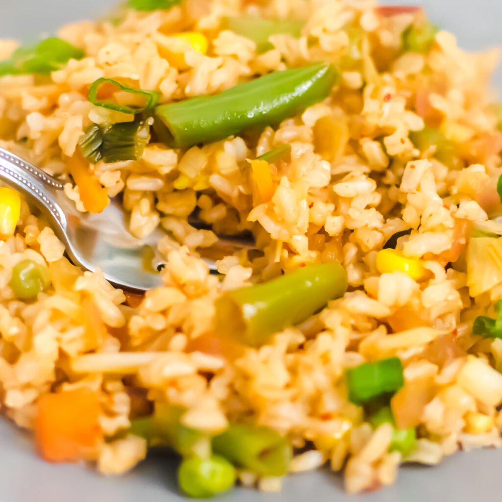 a close up view of schezwan fried rice with a fork digging into it. 
