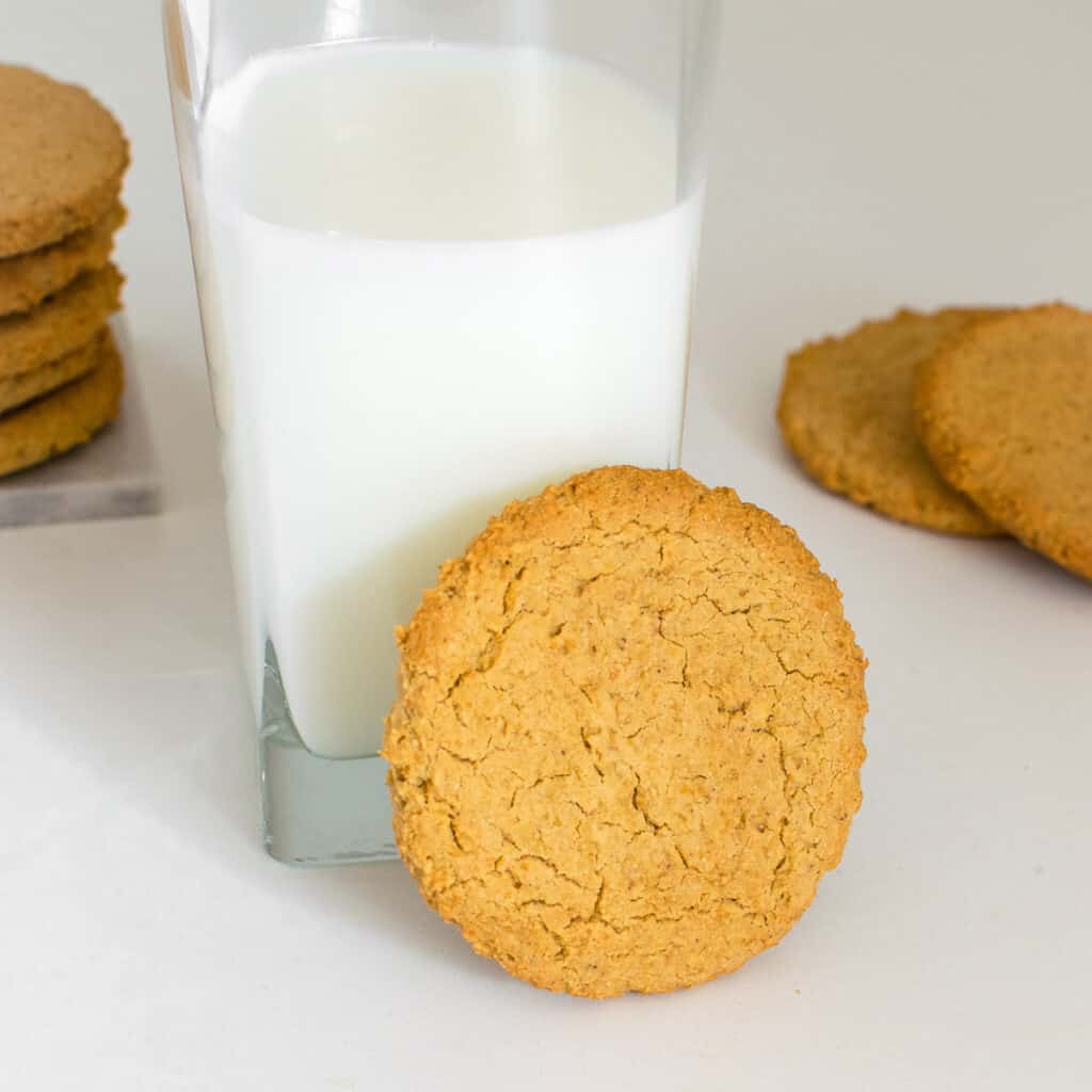 a chickpea cookie in focus supported by a milk glass