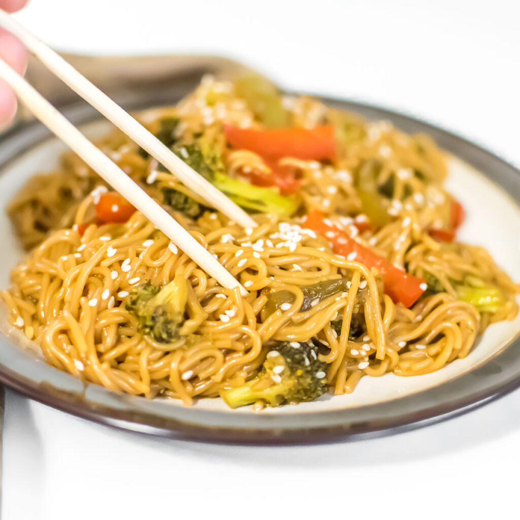 a hand picking up teriyaki noodles with the help of chopsticks. 