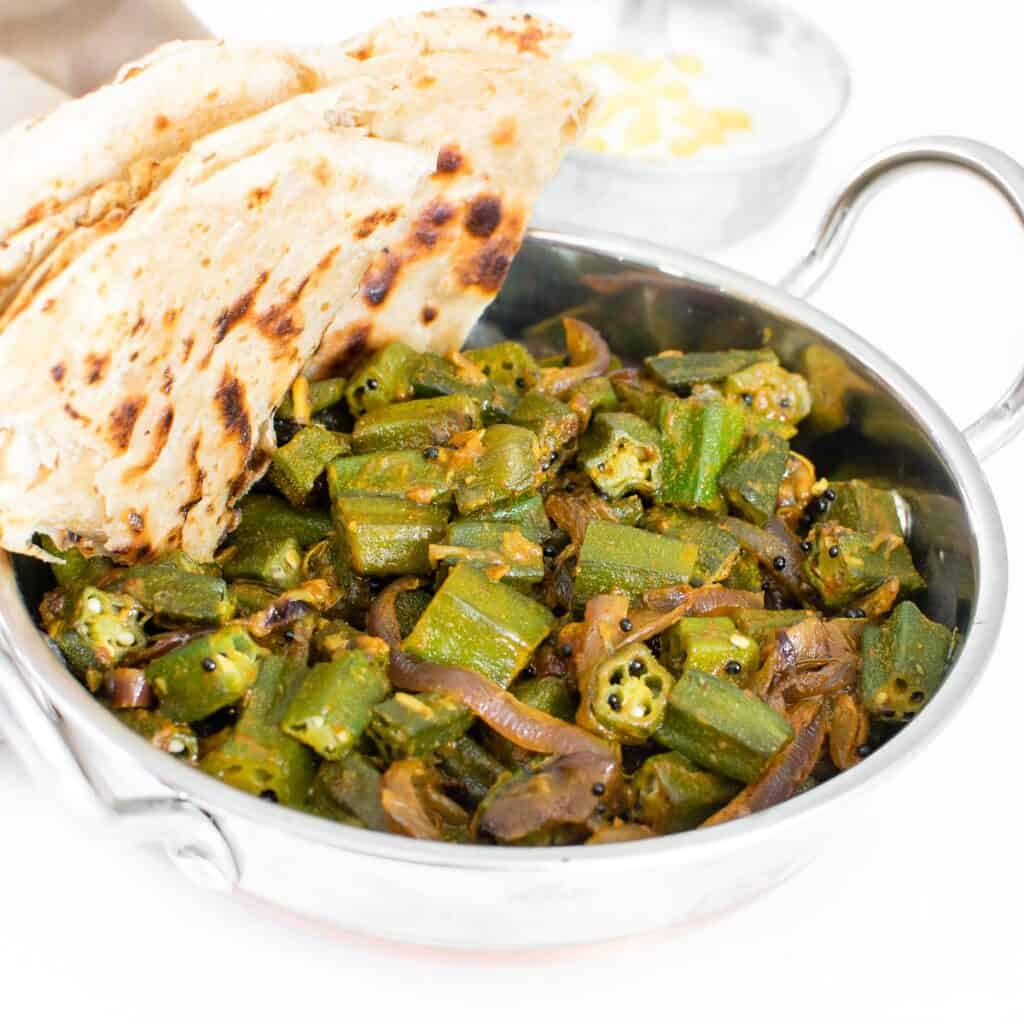 a 45 degree angle view of served bhindi masala in a kadhai with rotis.