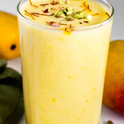 front view of vegan mango lassi in a serving glass with garnishes.