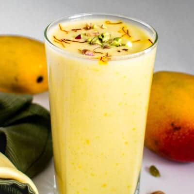front view of vegan mango lassi in a serving glass with garnishes.