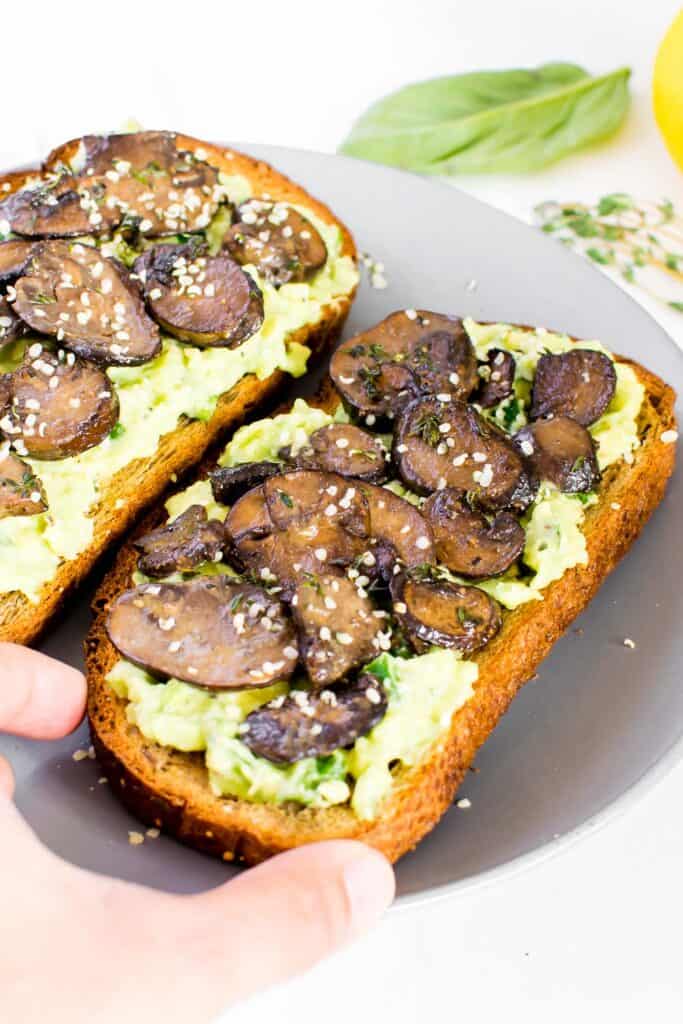 a close up view of a hand picking up a slice of mushroom avocado toast.