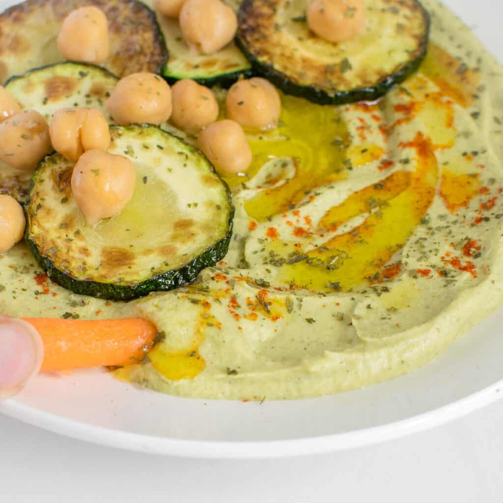 a close up view of a carrot dipping in zucchini hummus.