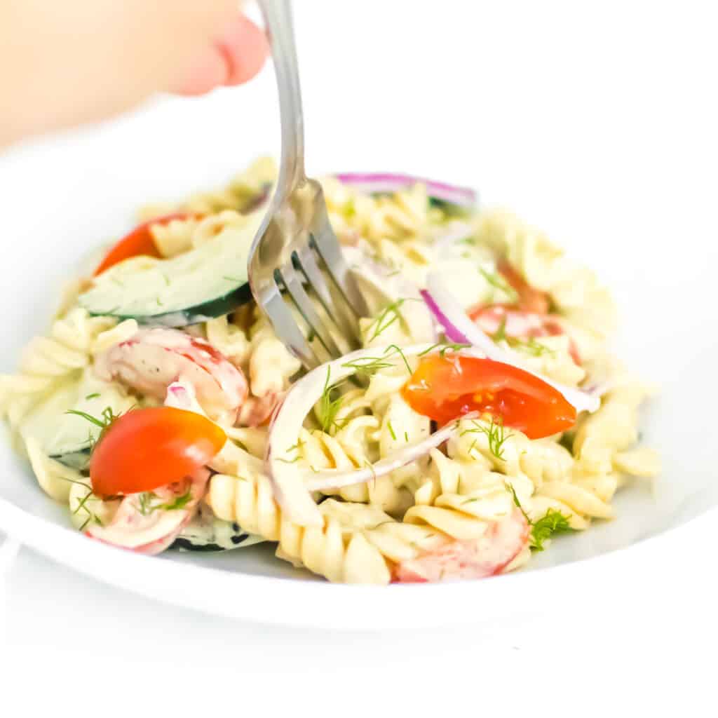 a fork digging into tomato cucumber pasta salad. 