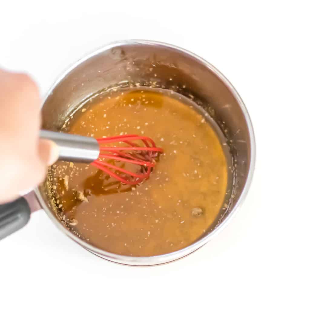 a hand whisking maple syrup in the saucepan.