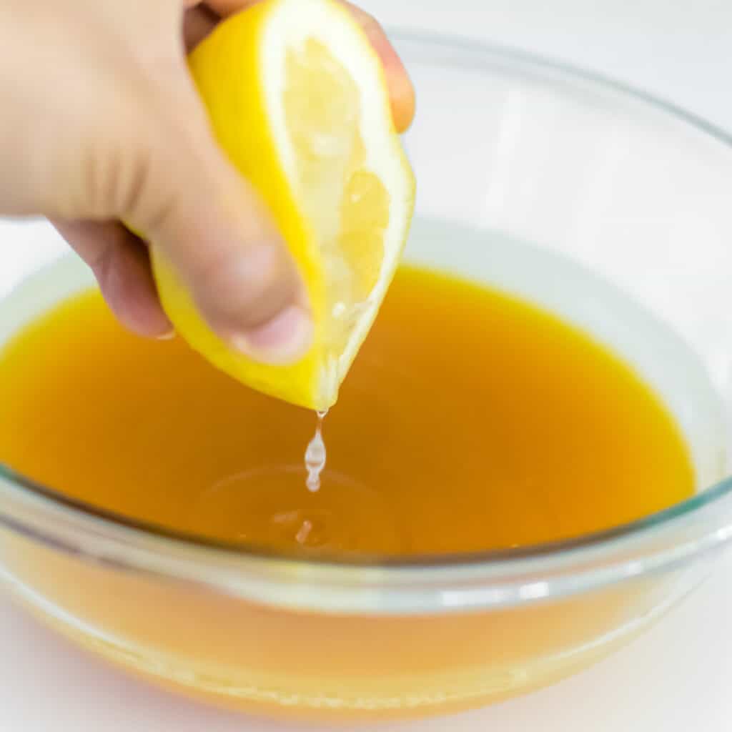 a hand squeezing fresh lemon into the lemonade. 