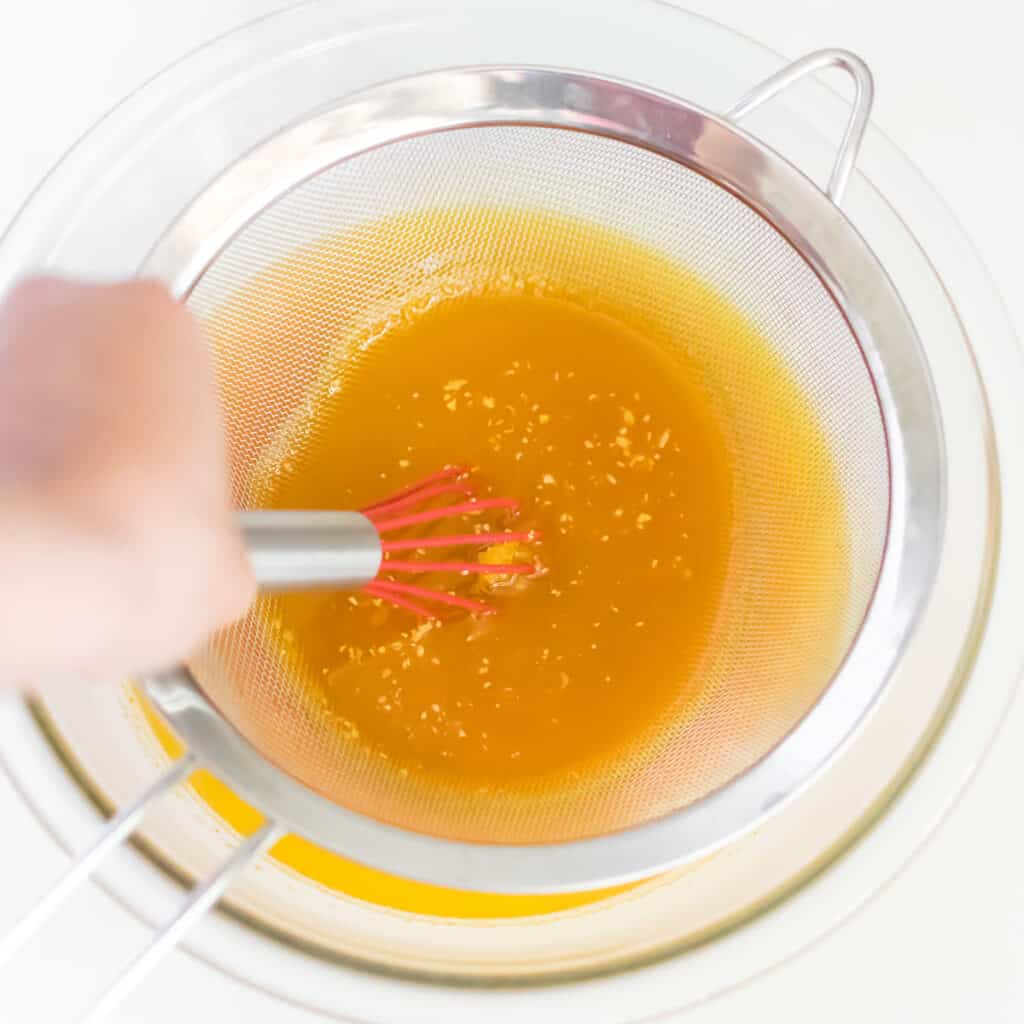 a hand whisking turmeric water through the strainer. 