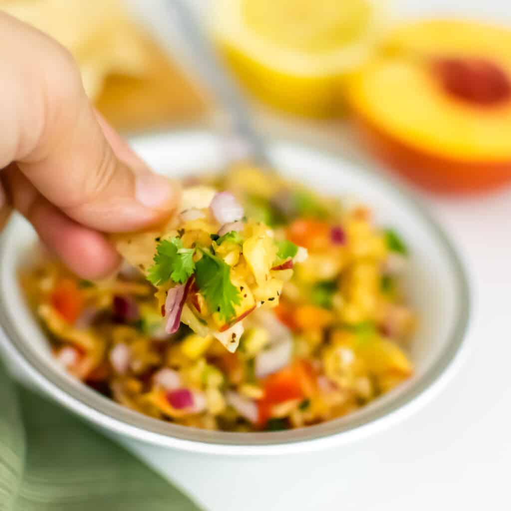 a hand showing chips filled with peach salsa.