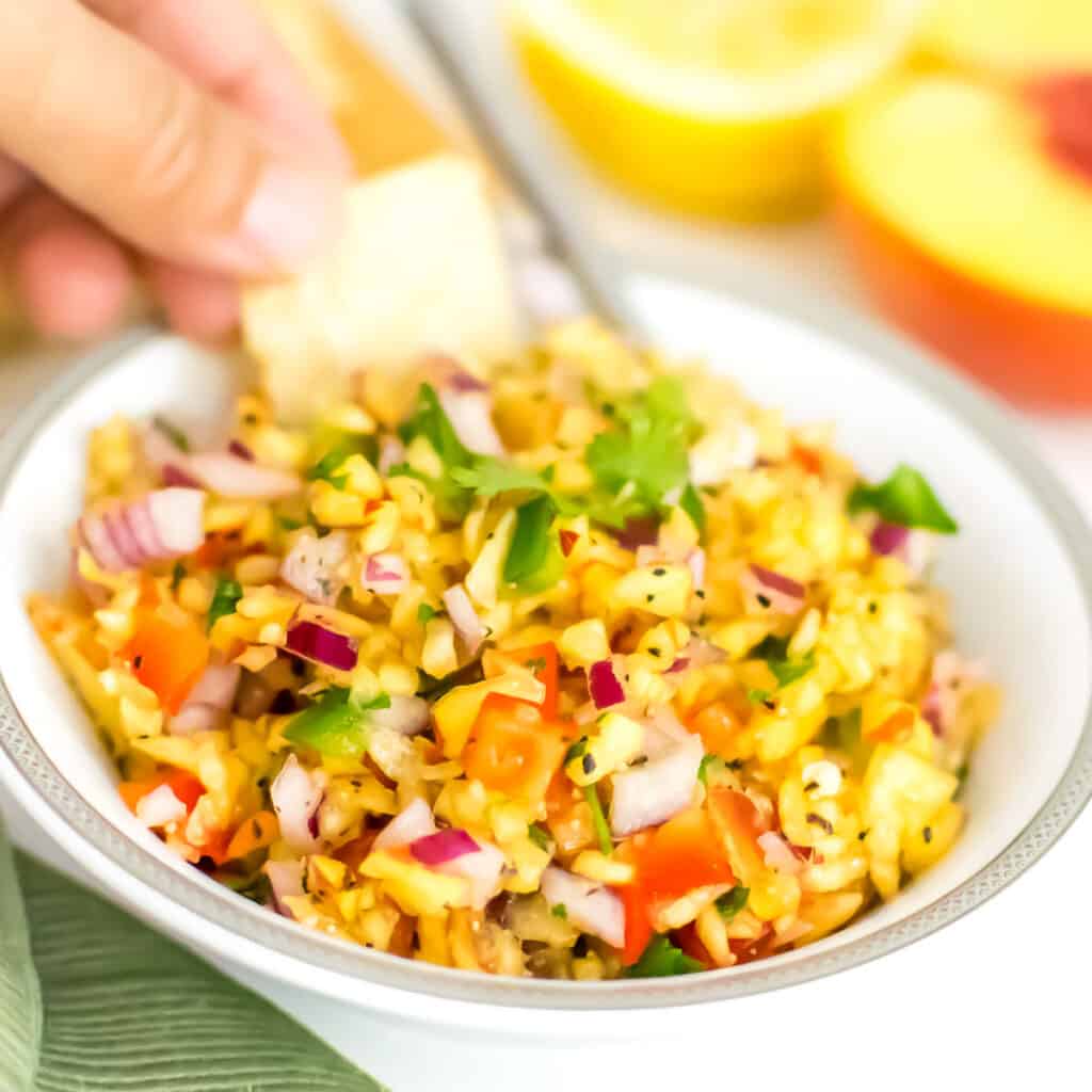 a hand holding chips and digging into peach salsa.