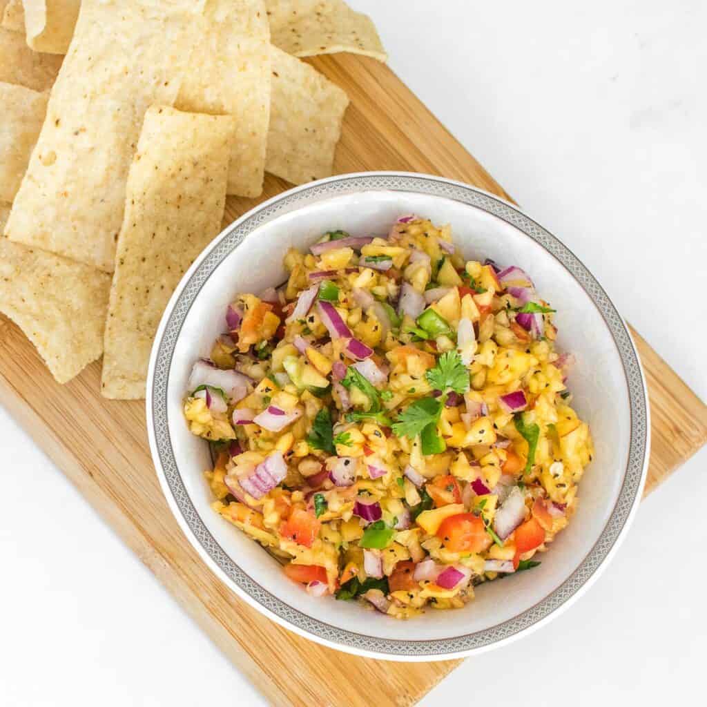 top view of served peach salsa on wooden board with chips. 