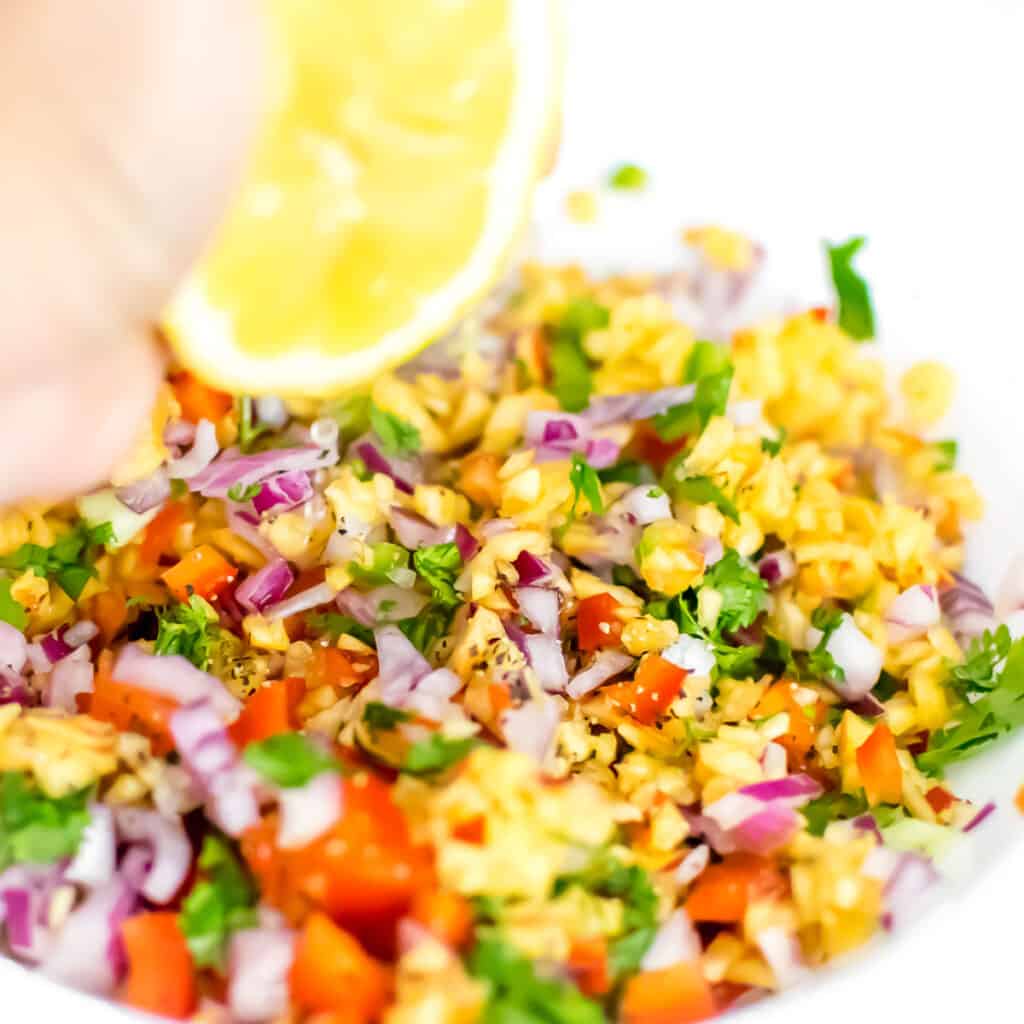 hand squeezing lemon over the ingredients in the bowl. 