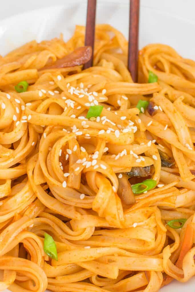 a close up view of gochujang noodles wrapped in a pair of chopsticks. 