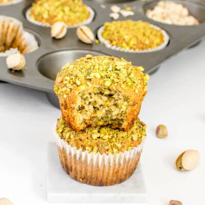 half eaten pistachio muffin stacked on top of another muffin with its tray at the background.
