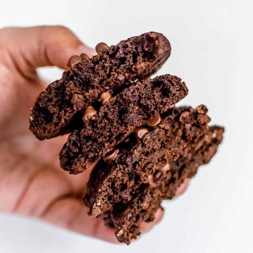a hand holding a stack of halved vegan chocolate cookies. 