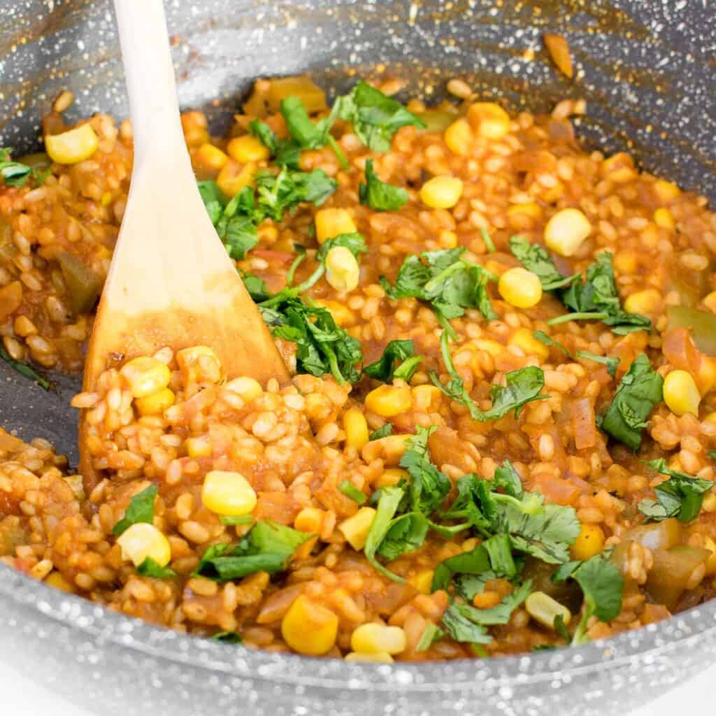 wooden spatula scraping and fluffing vegan Mexican brown rice. 