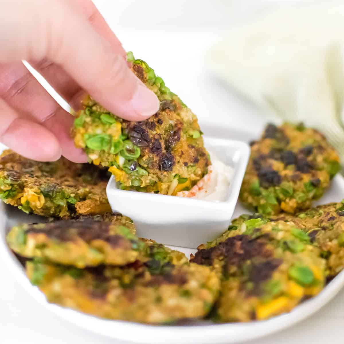 a hand holding one of the green pea fritters and dipping in the side dip. 