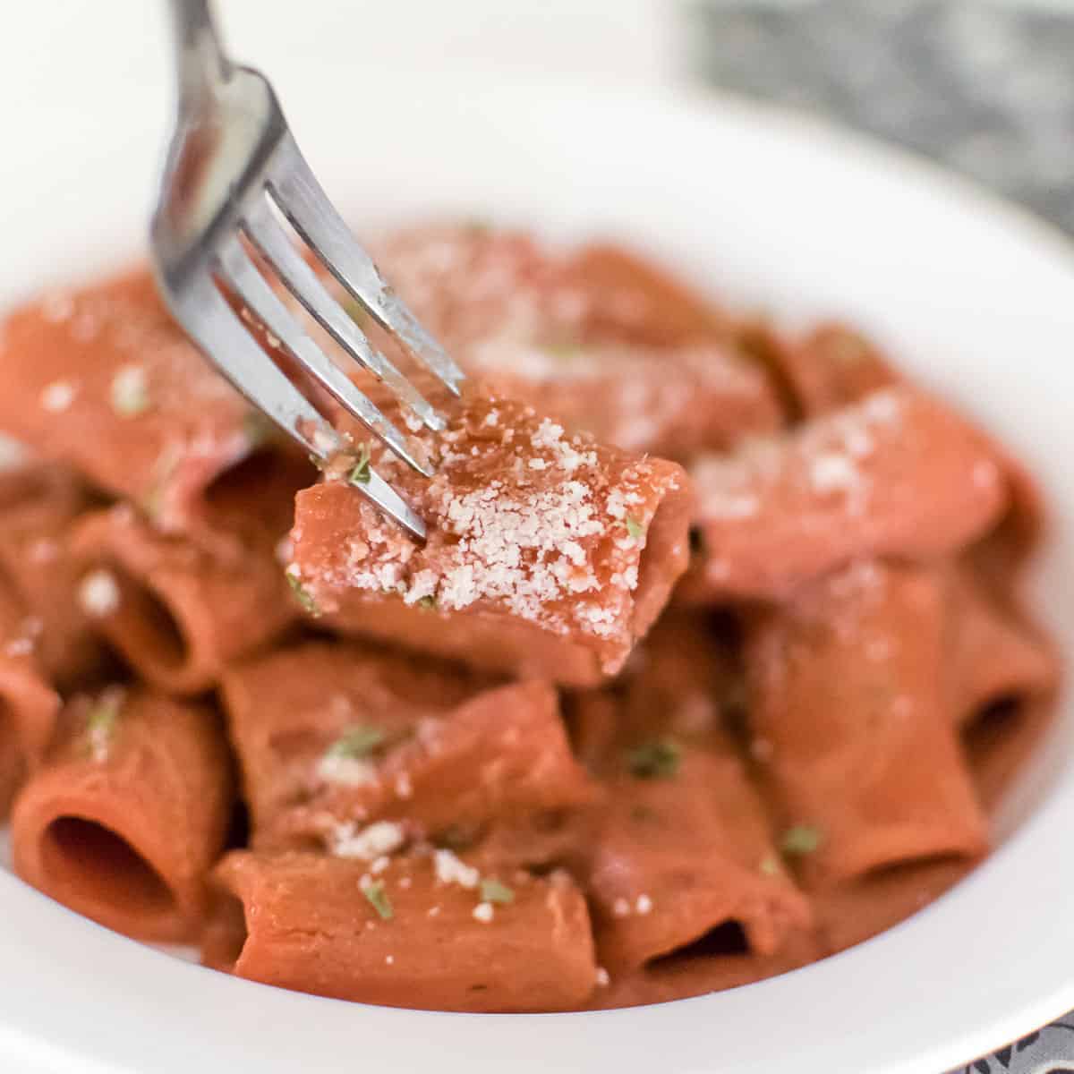 fork holing one of the beetroot pink sauce pasta from the plate. 