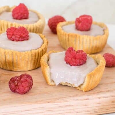 mini raspberry tarts on a wooden board with a focus on half eaten mini tart.