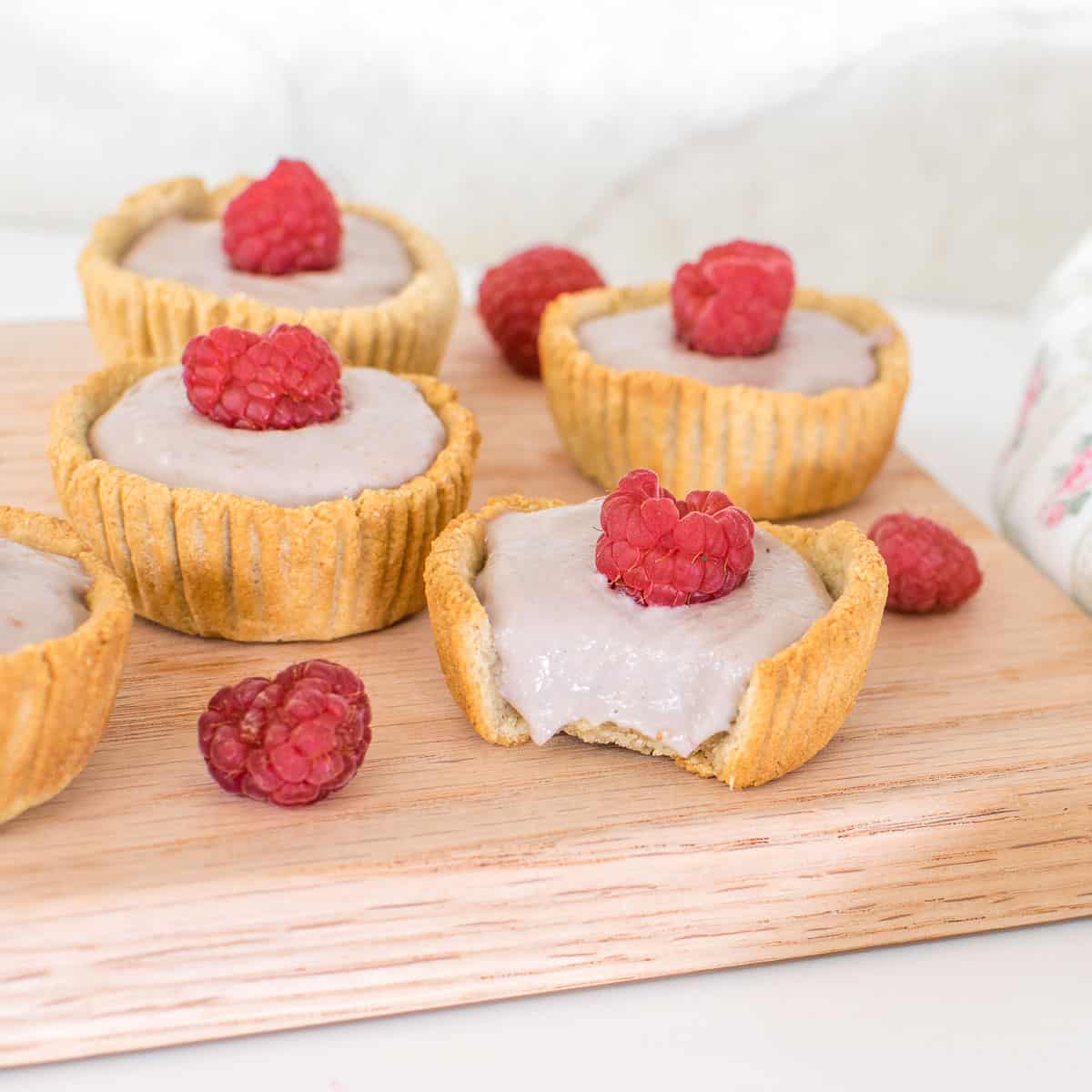 mini raspberry tarts on a wooden board with a focus on half eaten mini tart.