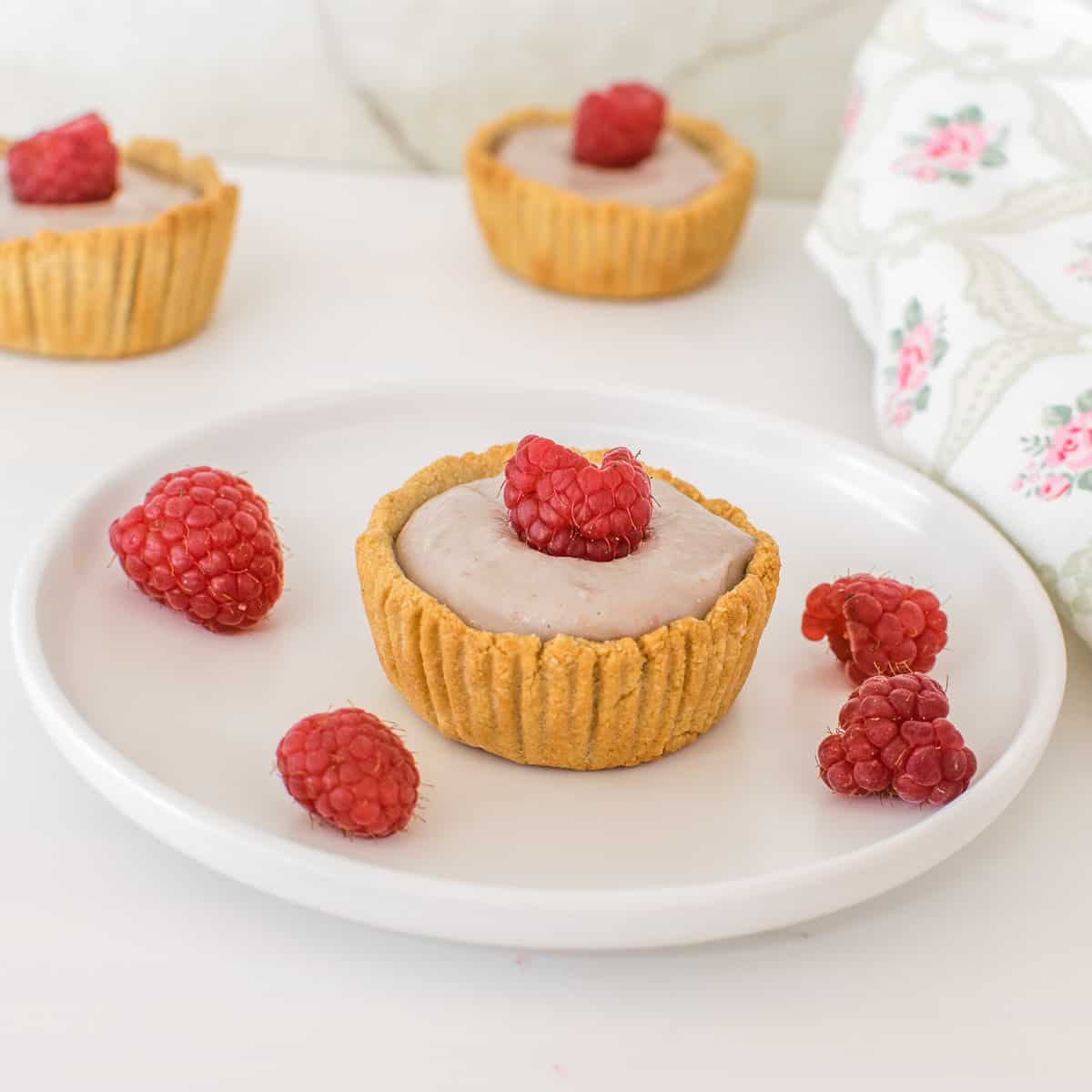 one of the mini raspberry cream tarts on a serving plate. 