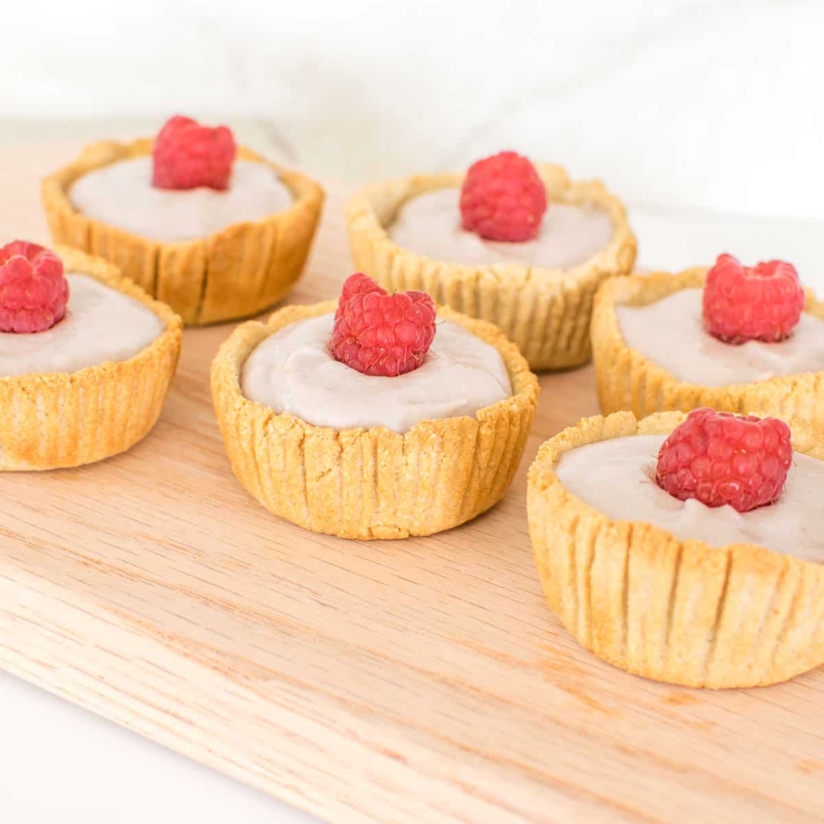 front view of vegan mini raspberry cream tarts on a wooden board. 