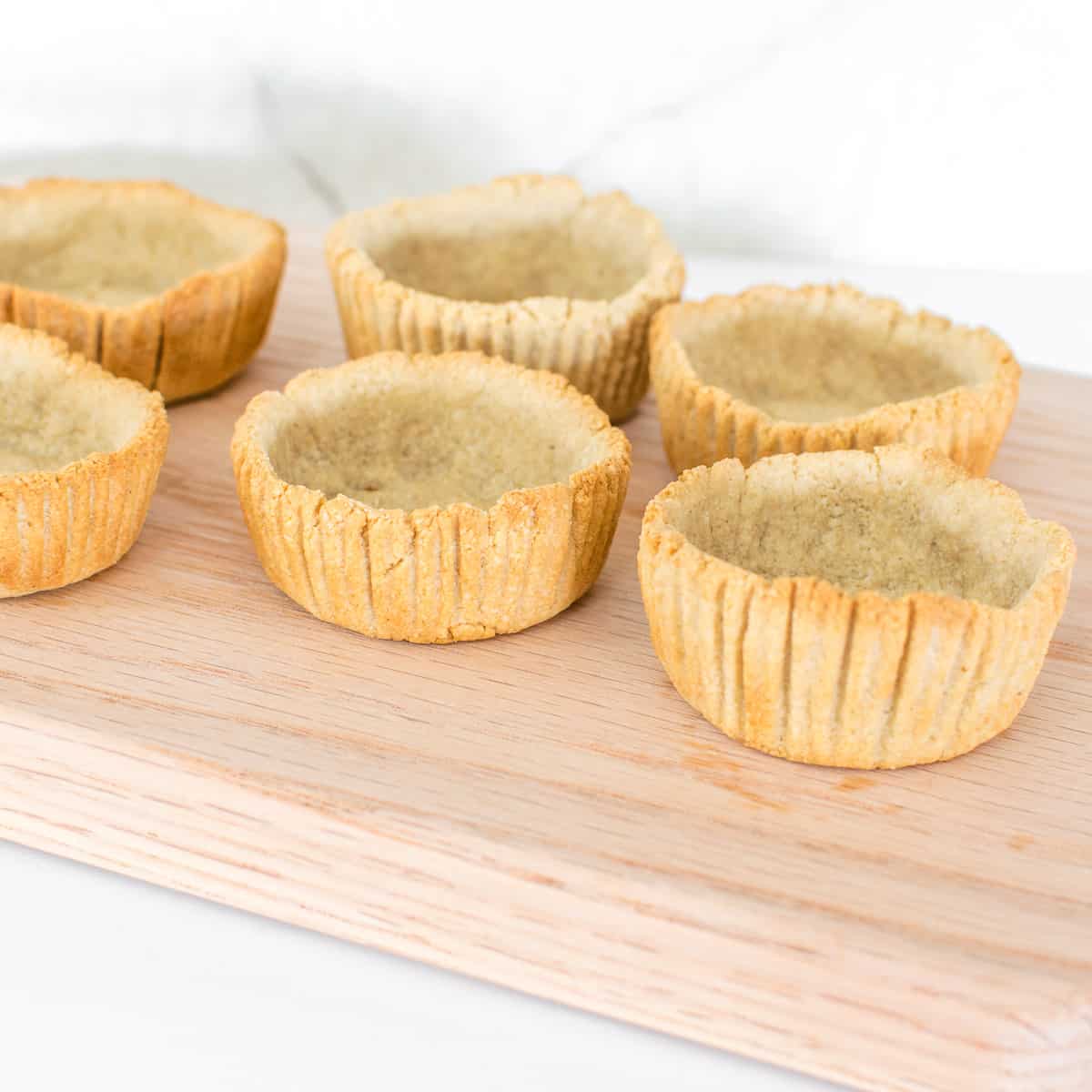 baked tart shells on a wooden board.