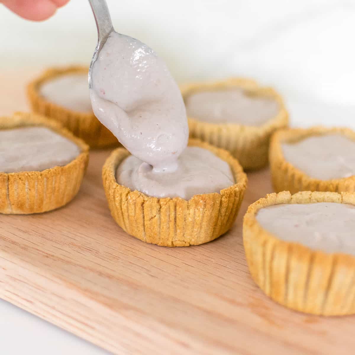 a hand pouring the filling into the tart shells with  spoon. 