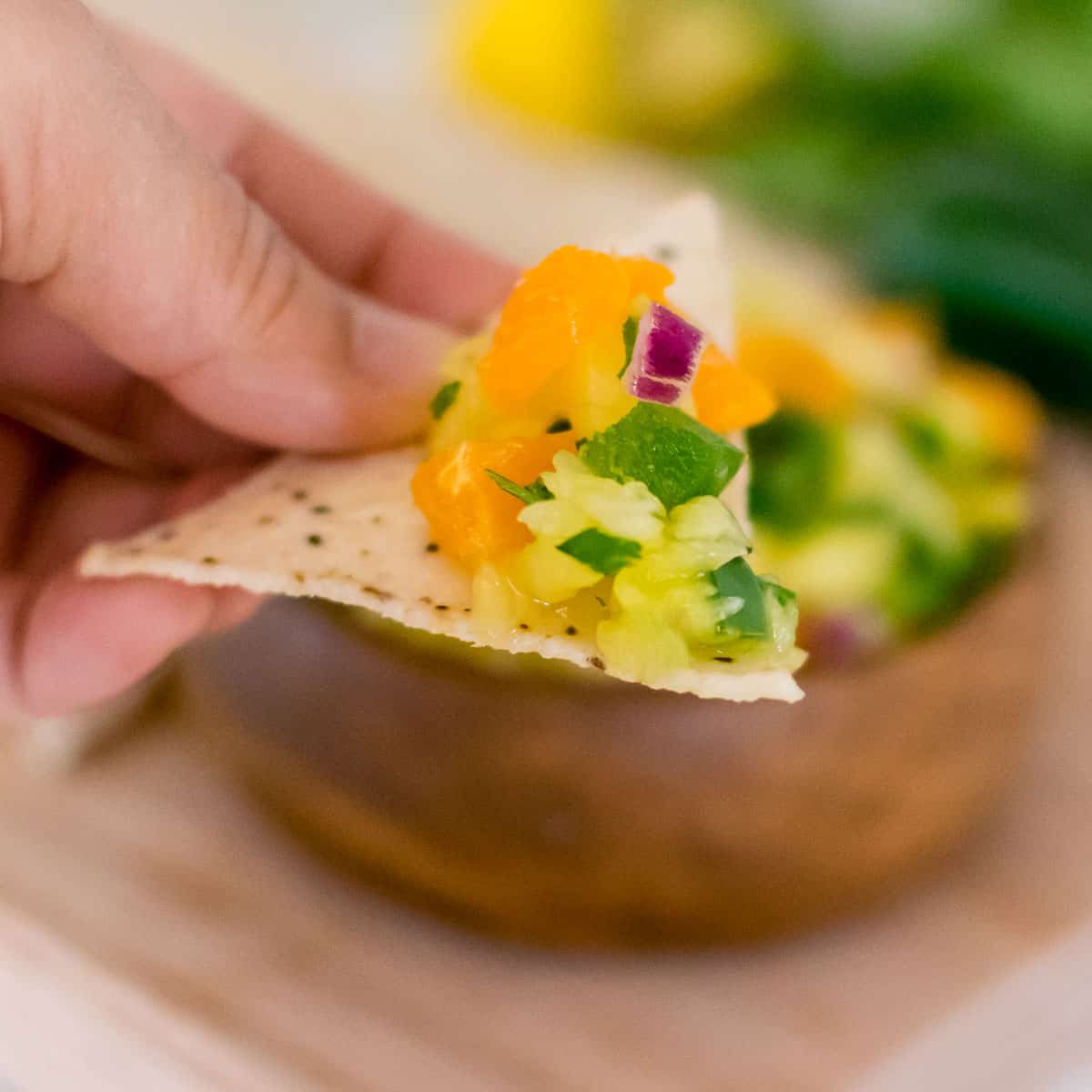 hand holding a chip with pineapple jalapeno salsa on it.