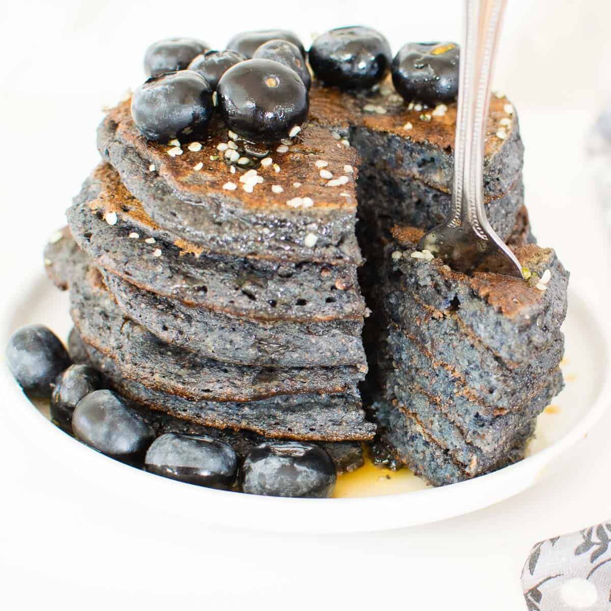 a fork digged into the slices of vegan blueberry spelt flour pancakes showing its inside. 