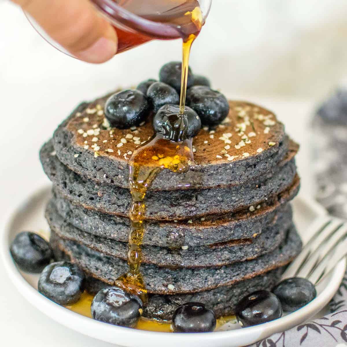 a hand drizzling maple syrup over the blueberry spelt flour pancakes.