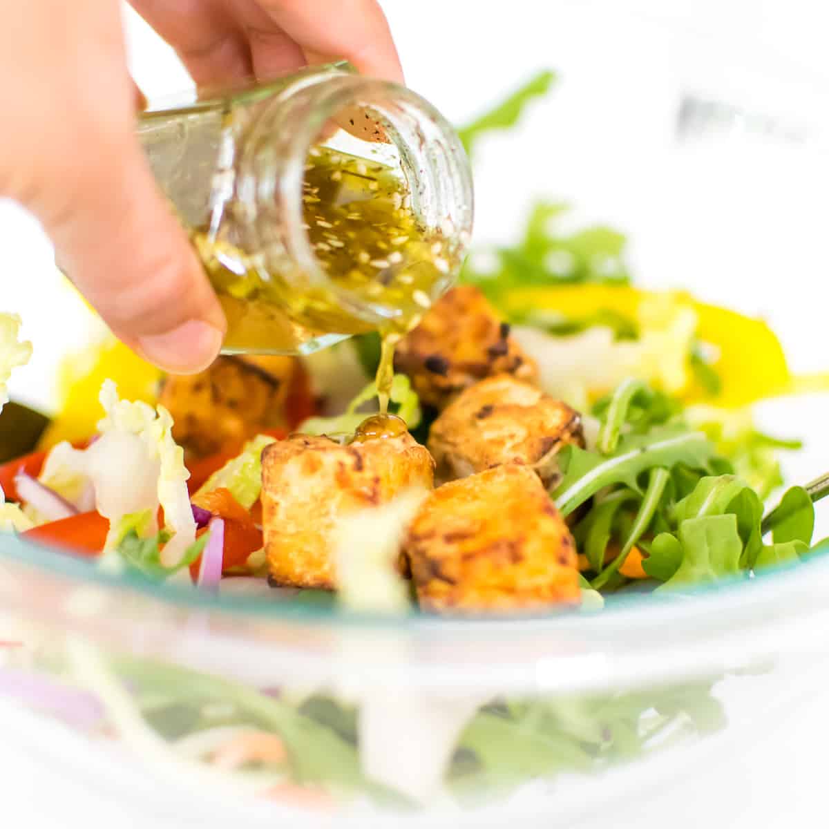 a hand holding the glass jar and drizzling the dressing over the salad. 