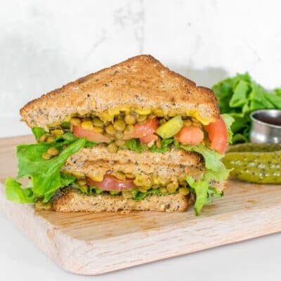 front view of stacked lentil sandwich on a wooden board with some sides and condiments.